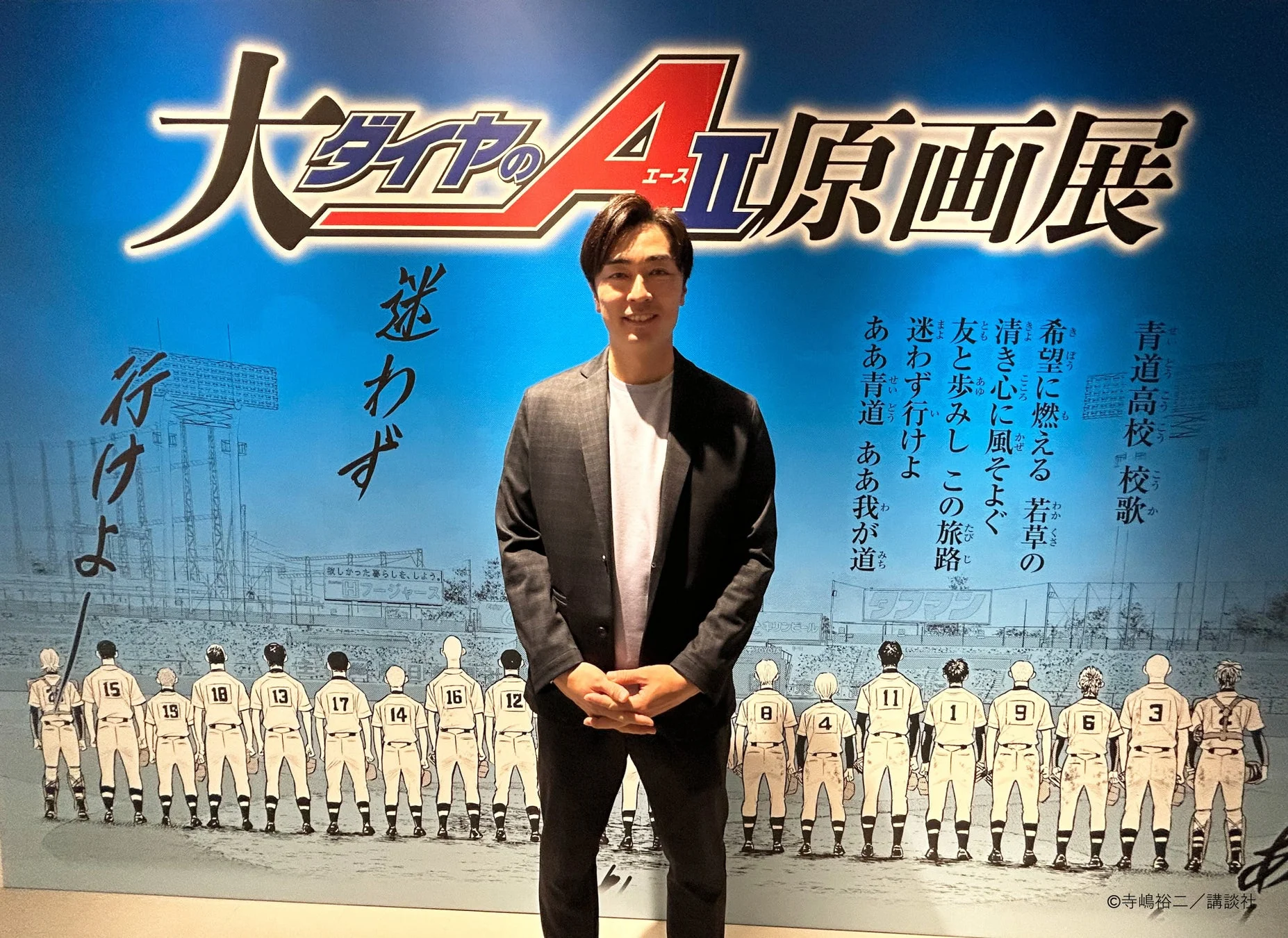 大『ダイヤのＡ actⅡ』原画展のポスターの前で笑顔を見せる和田毅氏