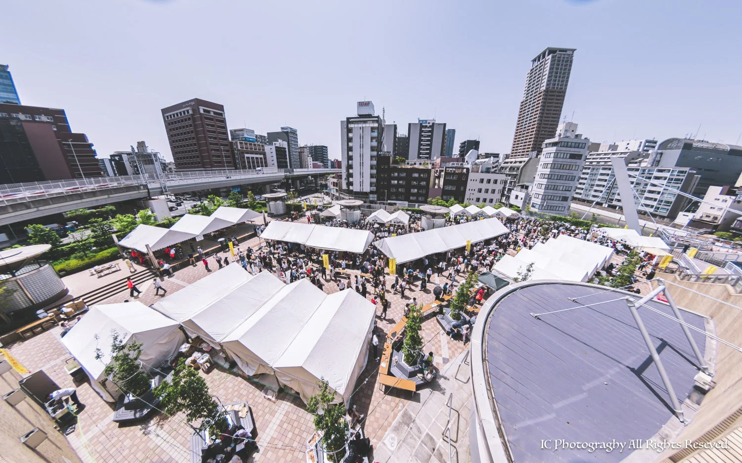 多くの白いテントが立ち並び、大勢の人々で賑わう屋外イベントの様子を上空から捉えた一枚