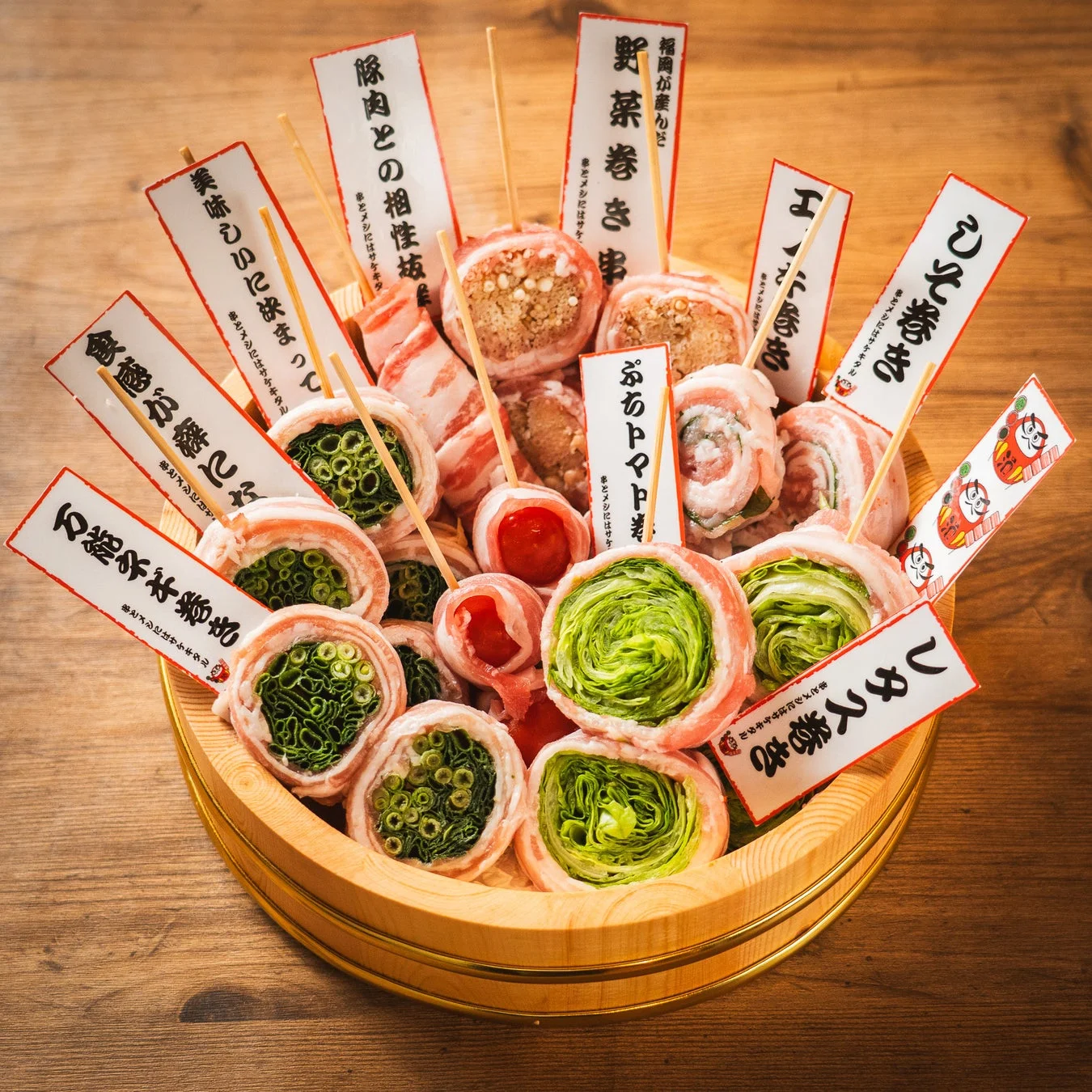 木製の桶に彩り豊かに盛り付けられた、豚肉で様々な具材を巻いた「豚肉巻き串」のセット