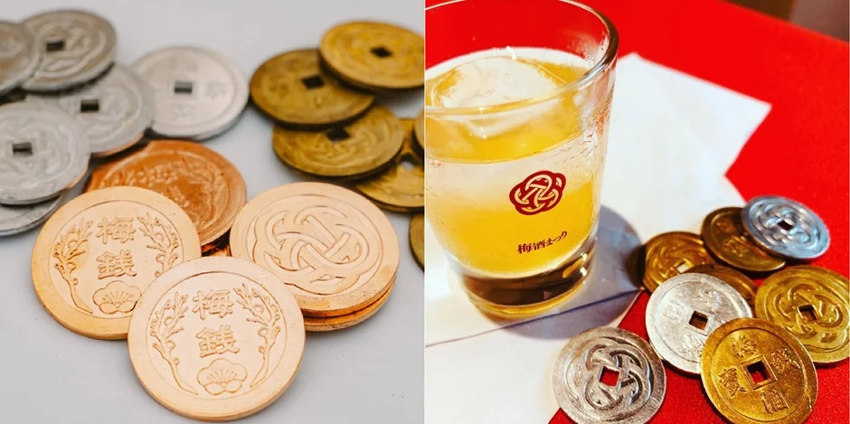 「梅銭」と書かれた和風のコインが複数散らばっており、隣には「梅酒まつり」のロゴが入ったグラスに梅酒が注がれている