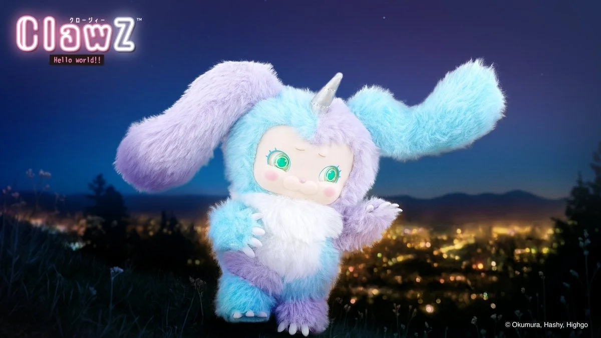 夜の丘の上に立つ、水色とラベンダー色の毛並みが特徴のユニコーンのような愛らしいキャラクターのぬいぐるみ