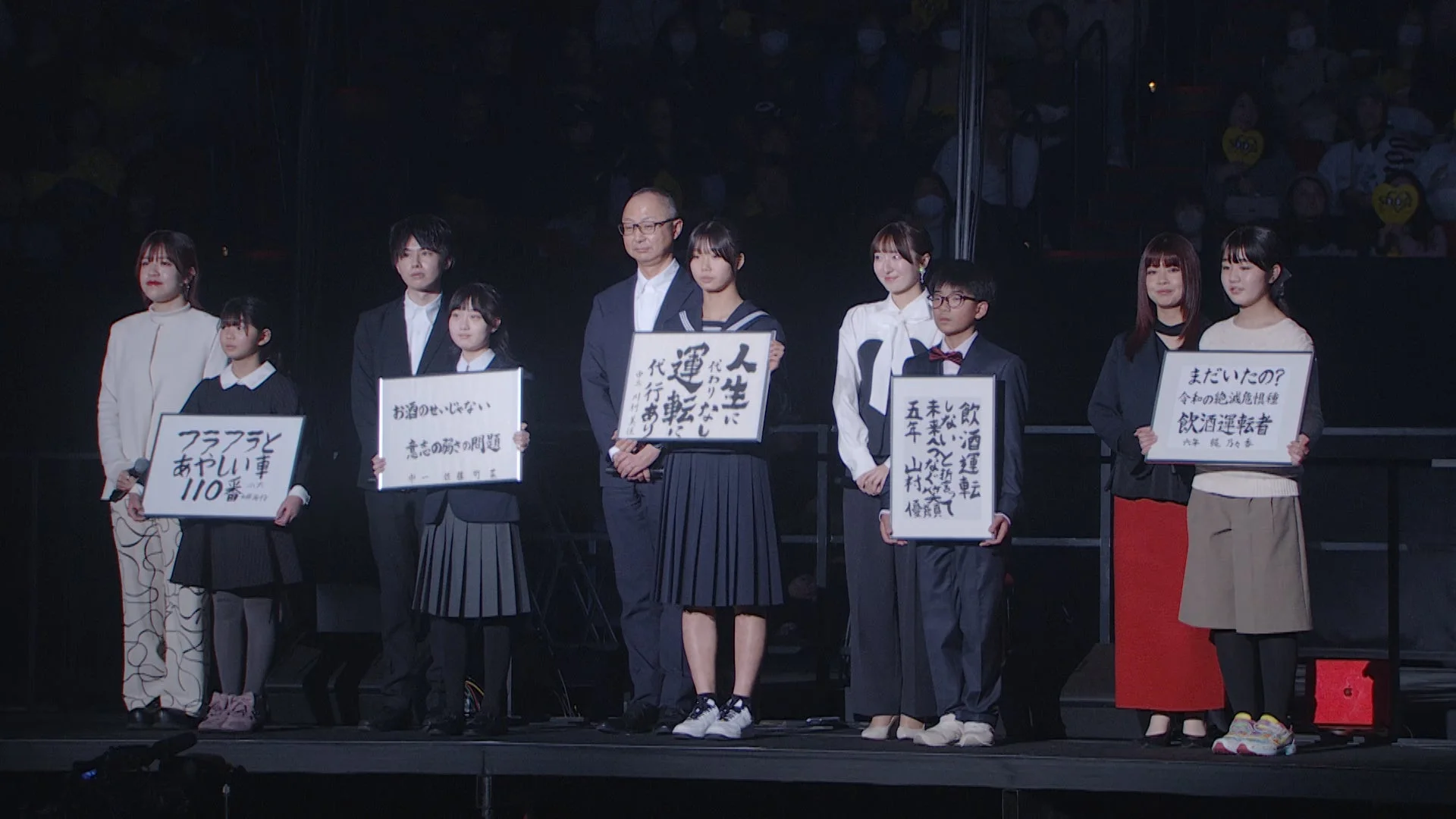 ステージ上の大人と子供たち、メッセージボード