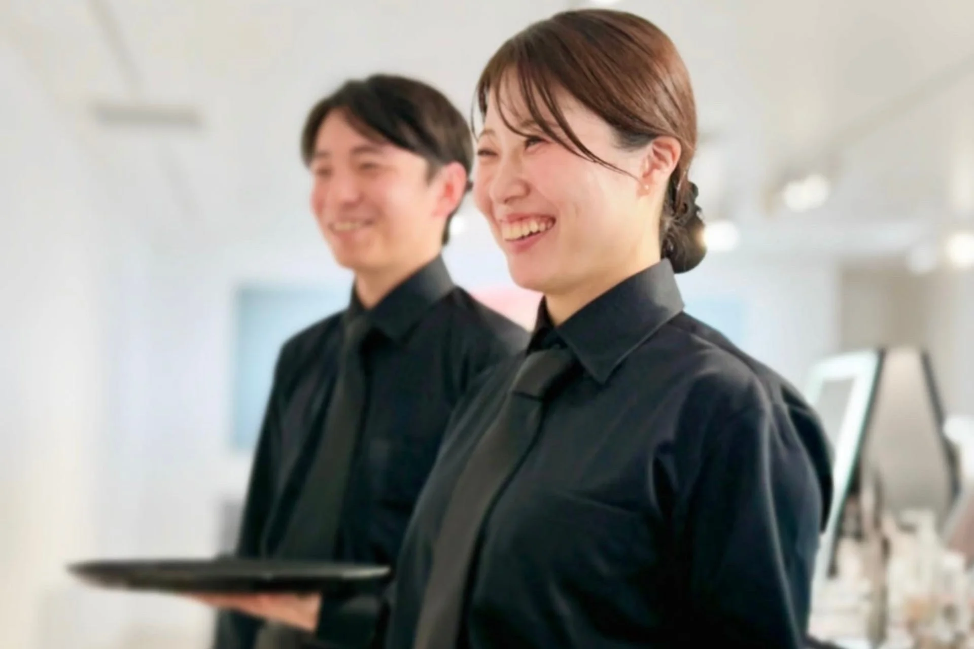黒い制服を着た男女のサービススタッフが笑顔で立っている様子