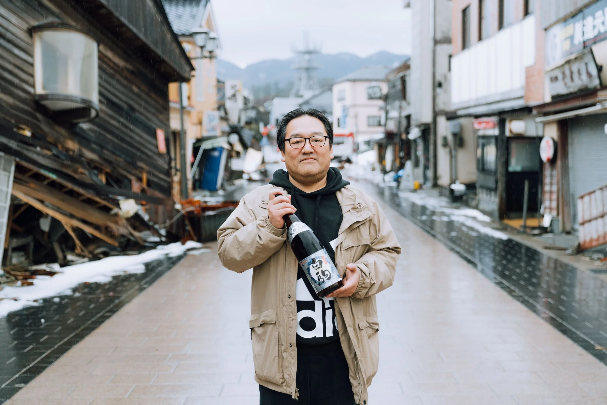 雪が残る日本の街並みで、一人の男性が「陸上55」と書かれた日本酒の瓶を手に立っている様子