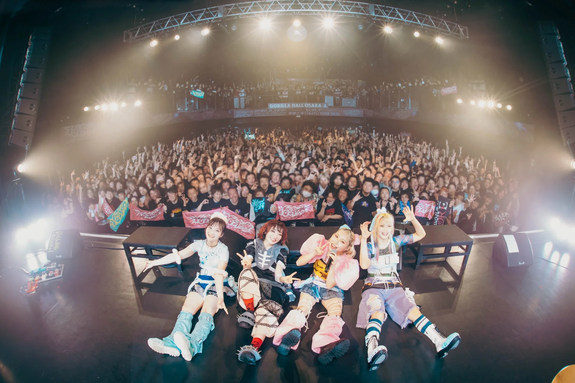 ライブ後のステージに座る4人組女性グループと熱狂的な観客