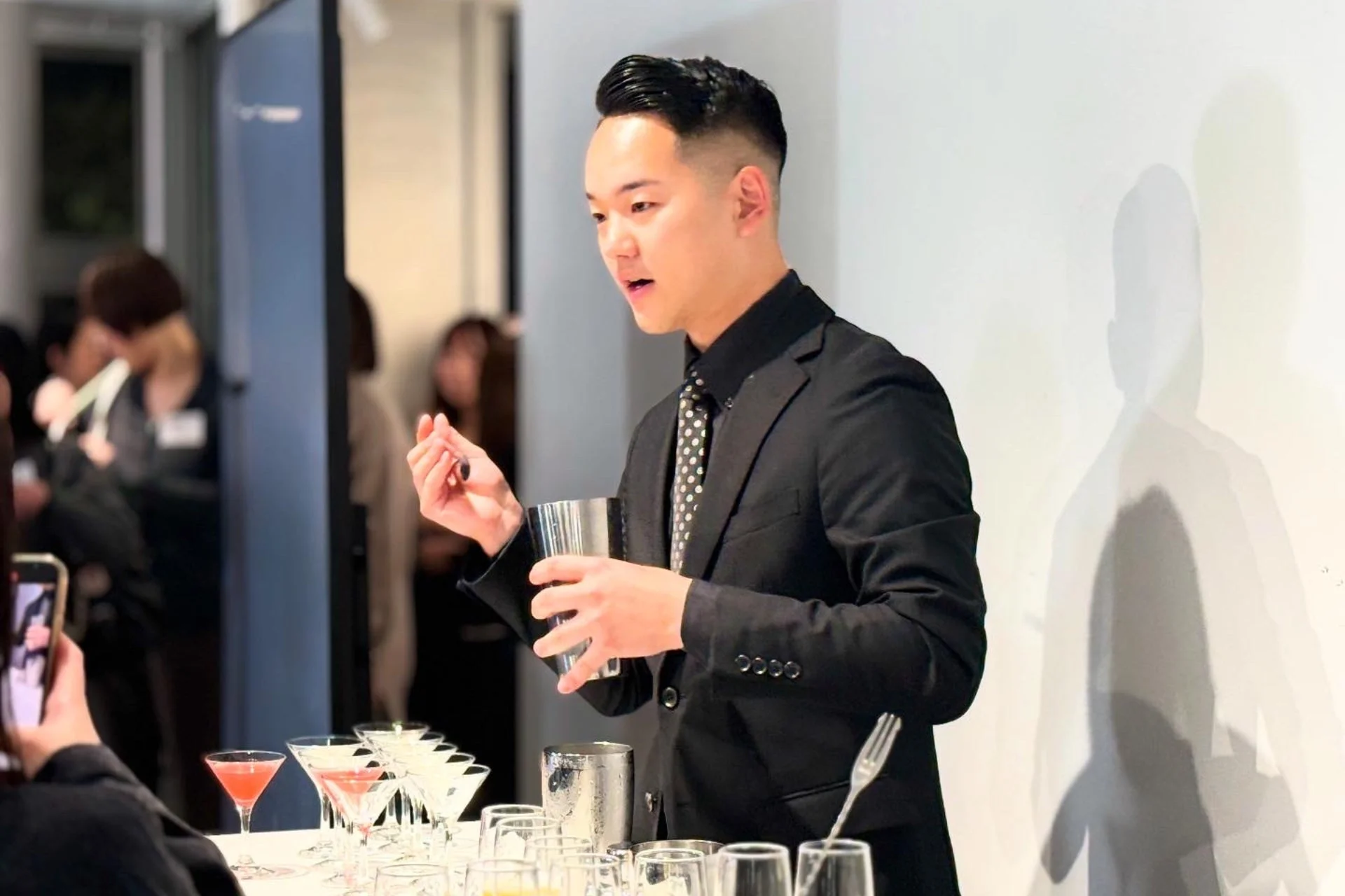 イベントで、スーツを着た男性バーテンダーがシェイカーを使ってカクテルを作っている様子