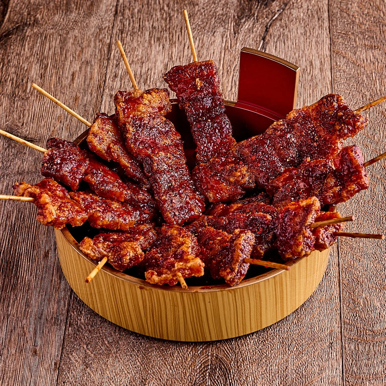木製の器に山盛りにされた、甘辛いタレがたっぷり絡んだ赤褐色の串焼き料理