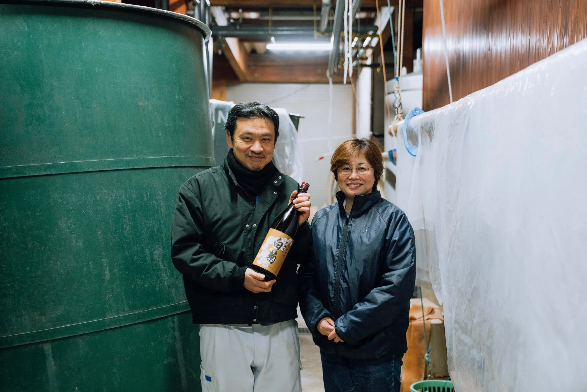 日本酒「白菊」のボトルを持つ男性と、その隣に立つ女性が笑顔で写っている