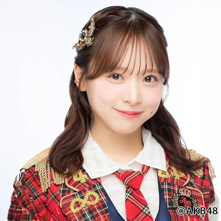 白い背景の前で笑顔を見せる若い日本人女性のポートレート。赤とチェック柄の華やかな衣装を着用し、ヘアアクセサリーを身につけている。