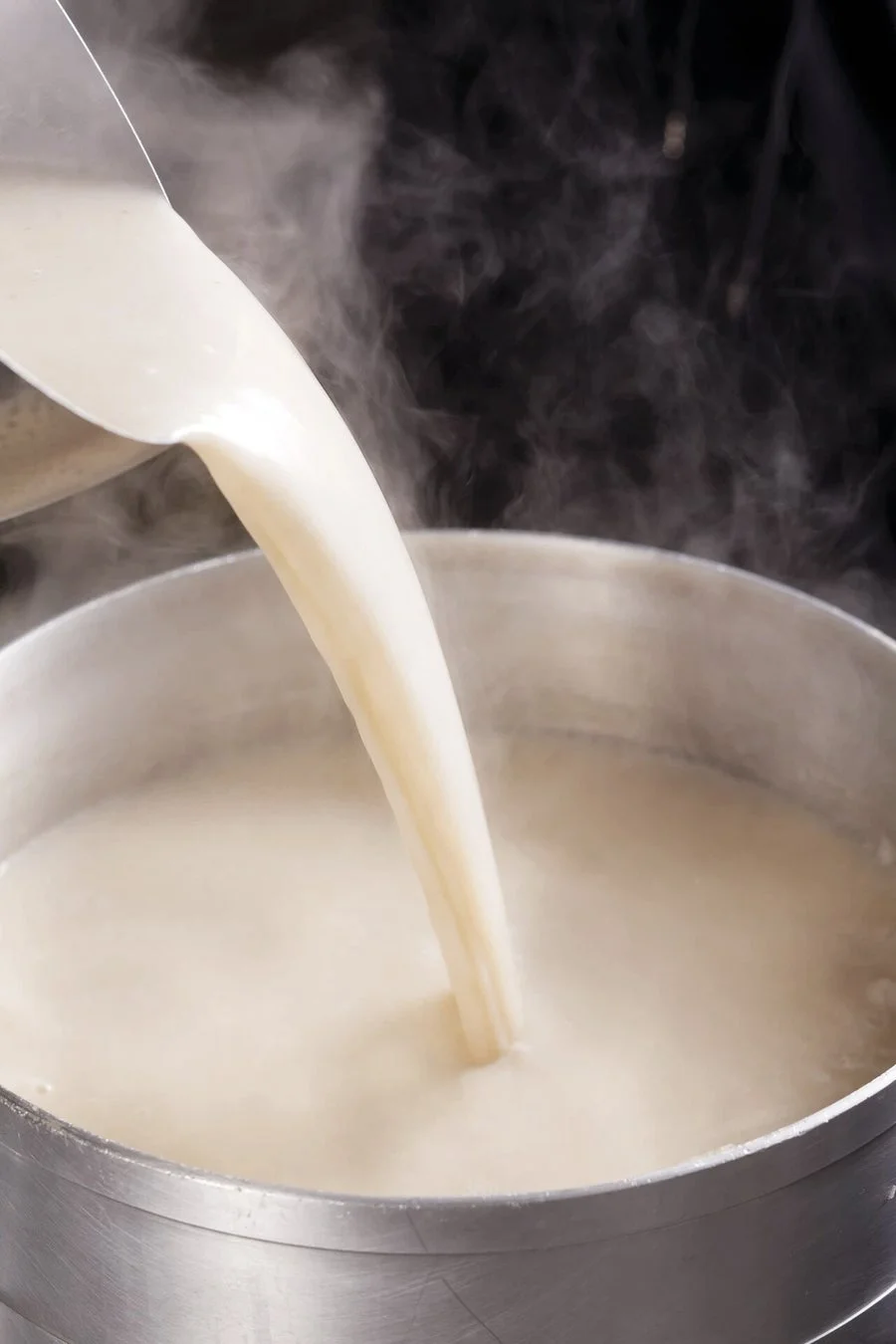 白いお玉から銀色の鍋に熱い液体が勢いよく注がれる様子