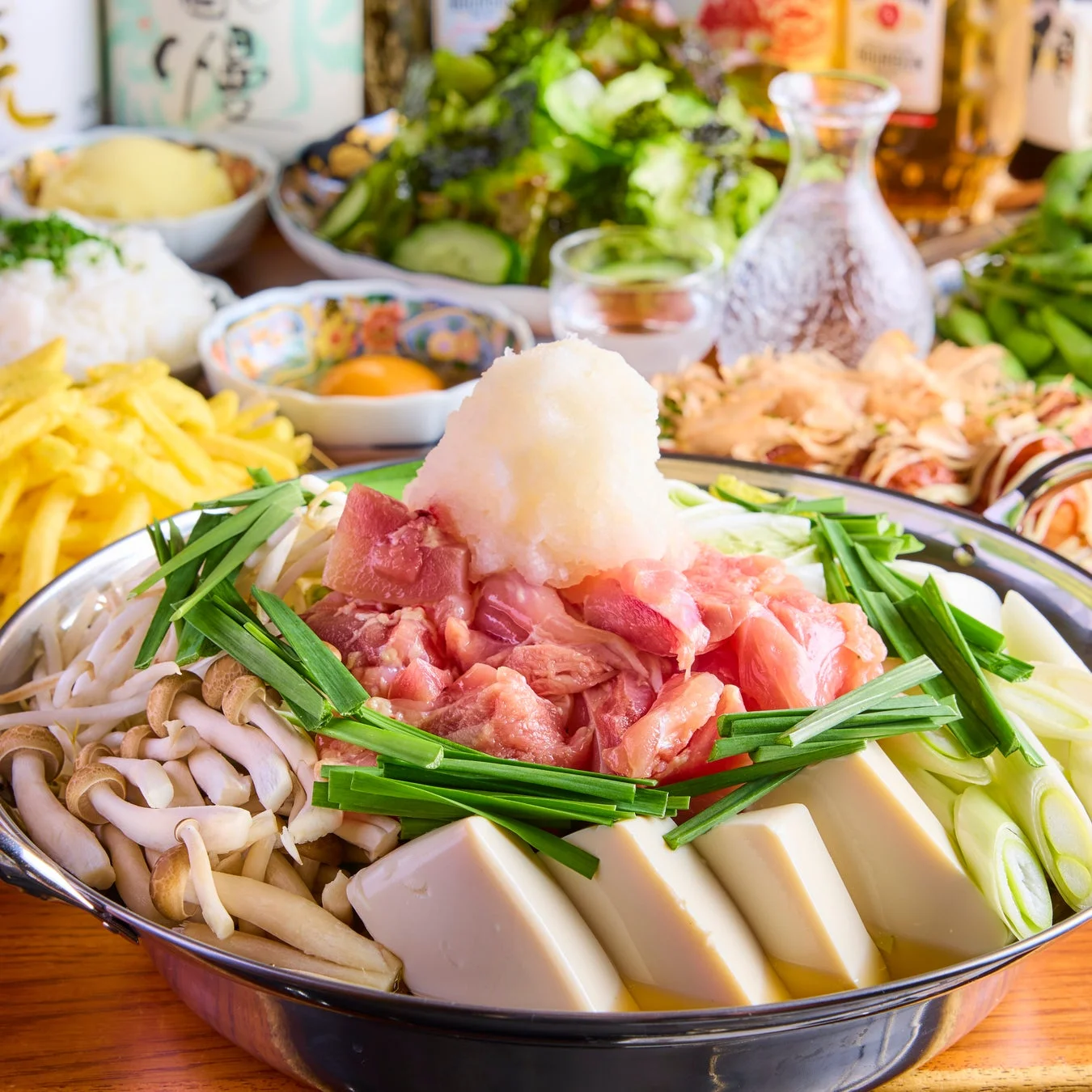 鶏肉、大根おろし、豆腐、きのこ、野菜がたっぷり入った鍋料理が中央にあり、フライドポテトやサラダ、生卵などのサイドメニューと共に食卓に並べられています