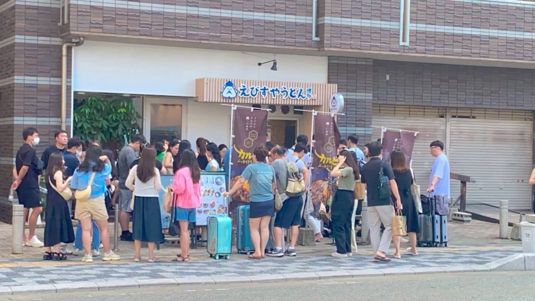 「えびすやうどん」と書かれた店の前に多くの人が行列を作る様子