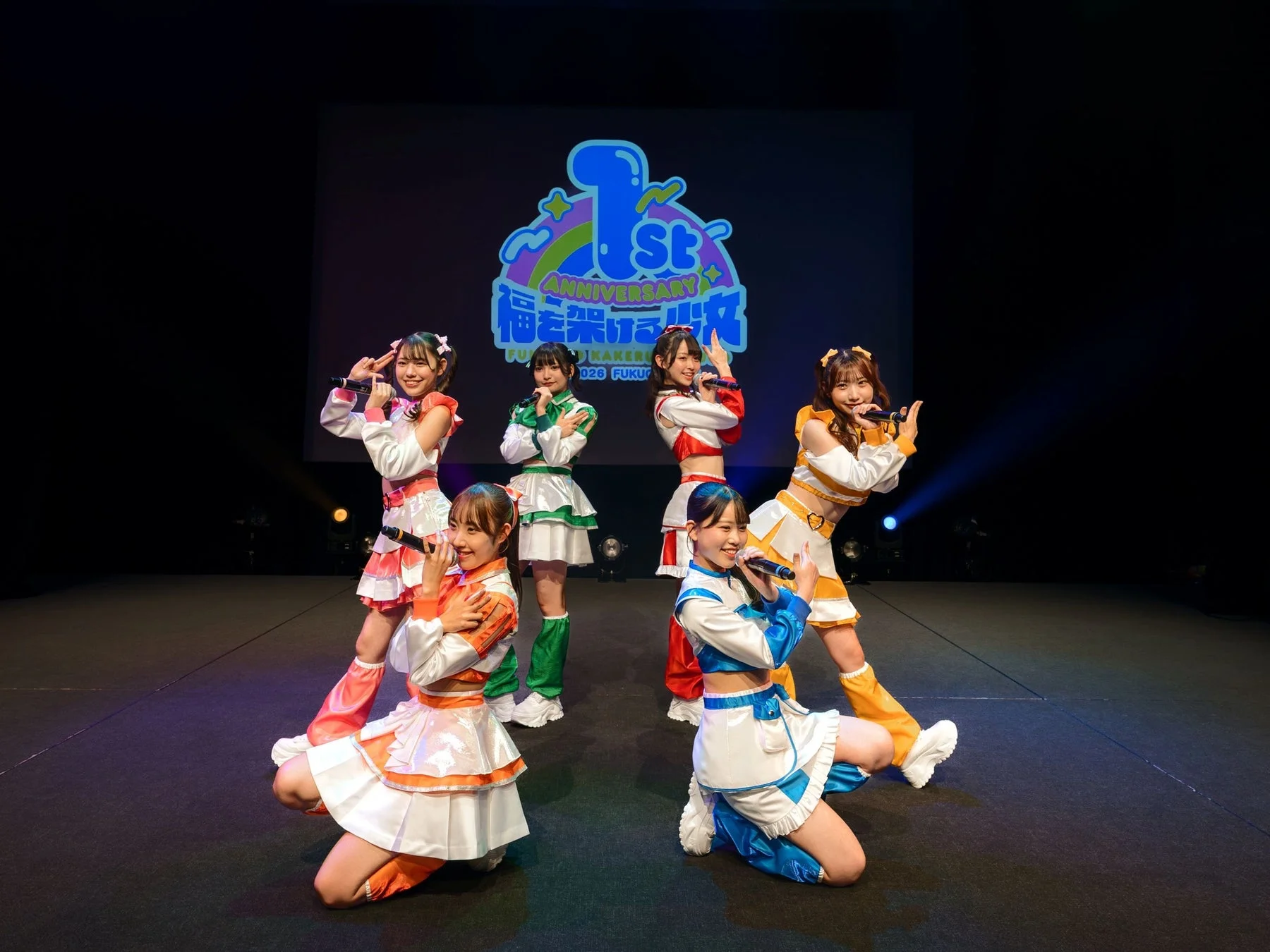 カラフルな衣装を纏った6人組アイドルグループがステージでパフォーマンスしている様子