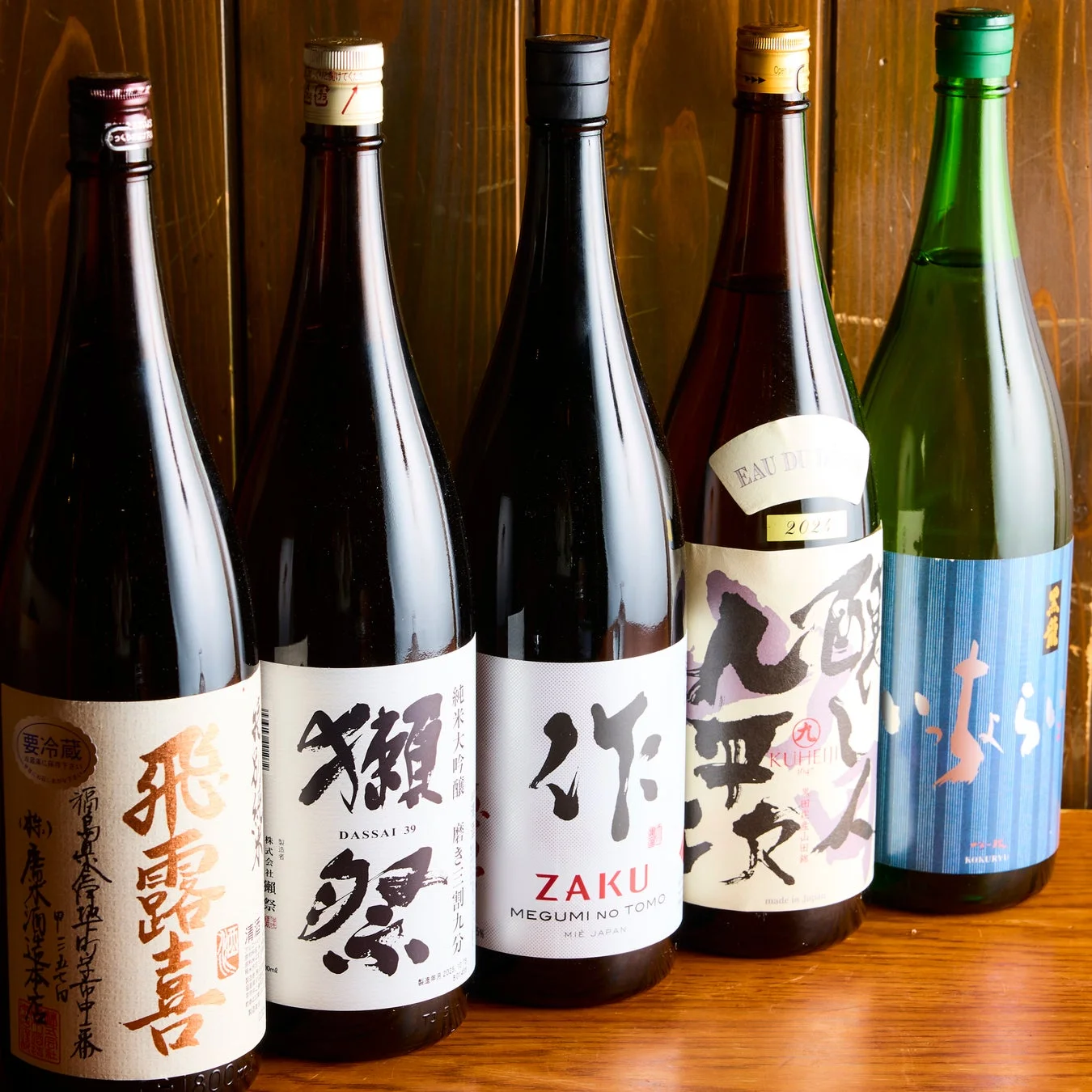 木製の背景とテーブルに、日本酒のボトルが5本並べられています