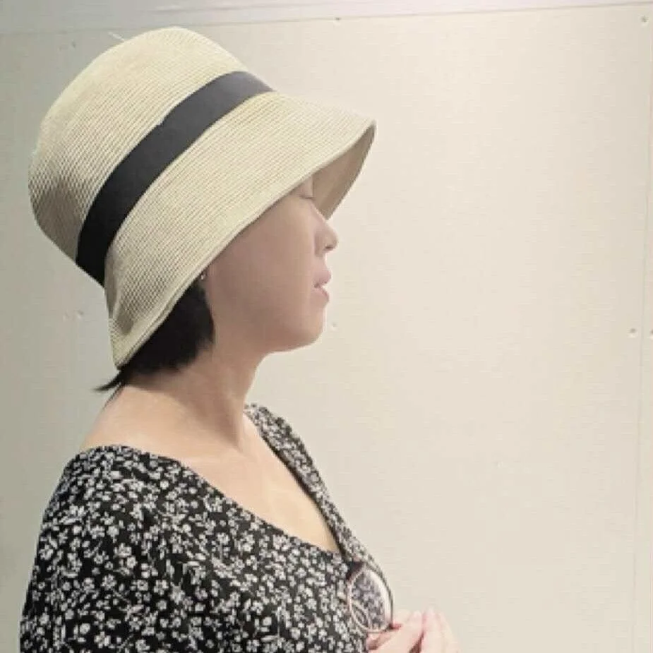 麦わら帽子と花柄のワンピースを着用した女性の横顔のポートレートです。帽子には黒いリボンがあしらわれています。