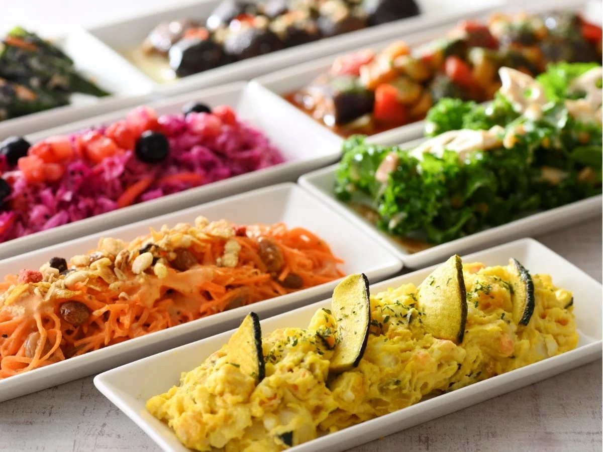 白い長皿に盛り付けられた、色とりどりのデリやサラダ