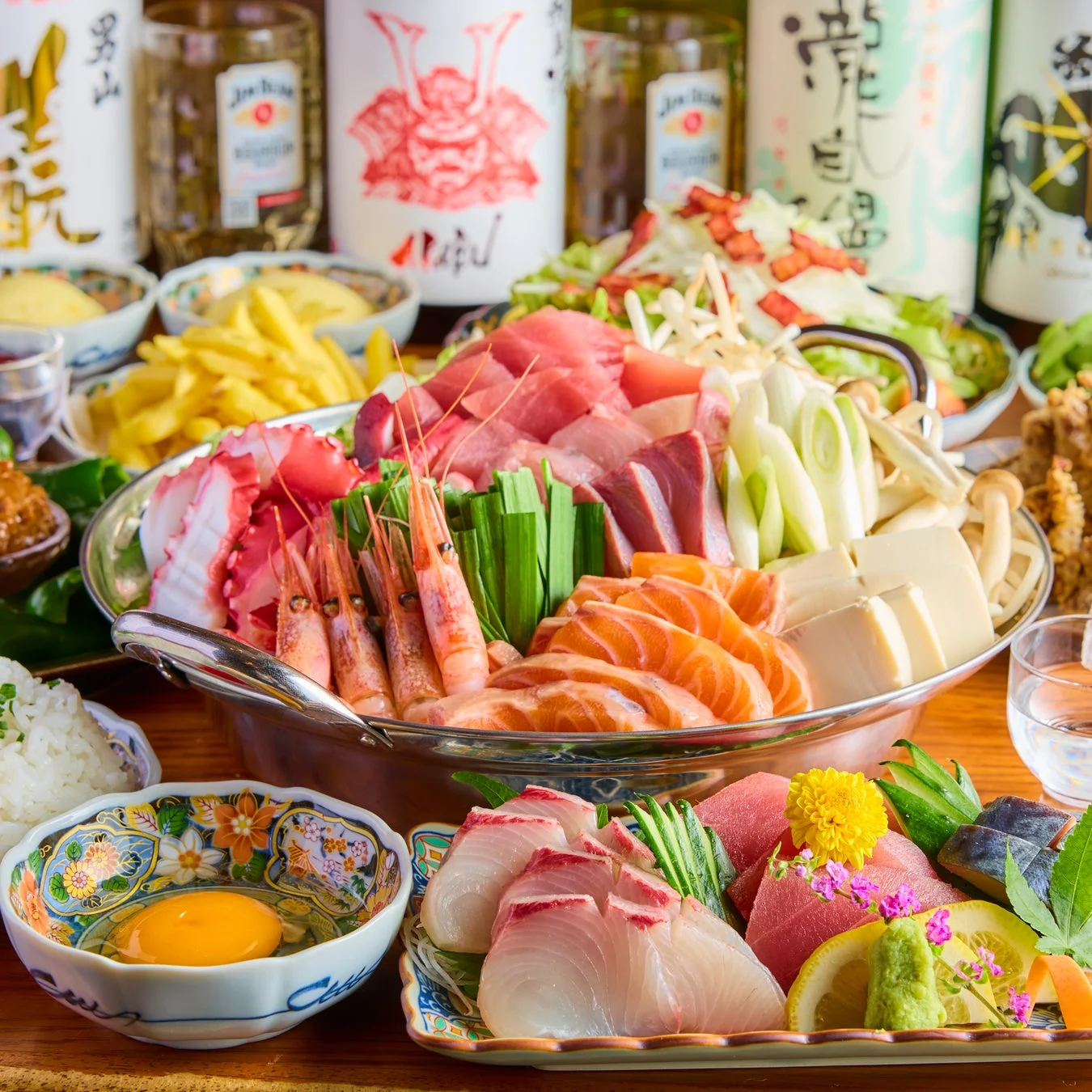 豪華な海鮮鍋が中心に置かれ、刺身、ご飯、生卵などが並ぶ和食の宴会風景