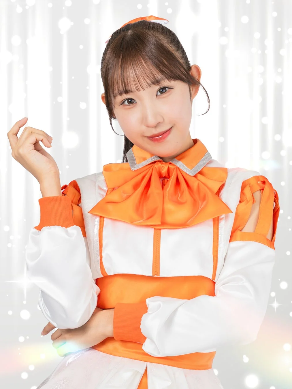 オレンジと白の可愛らしい衣装を着た若い女性が、笑顔でカメラに向かってポーズをとっているポートレート写真