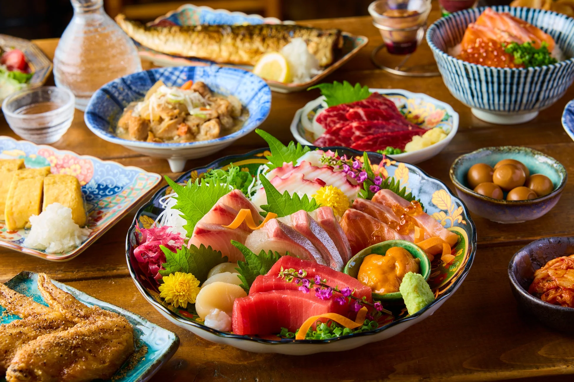 豪華な和食の食卓風景。新鮮な刺身の盛り合わせを中心に、焼き魚、いくら丼、玉子焼き、煮物、馬刺しなど多様な日本料理が並びます