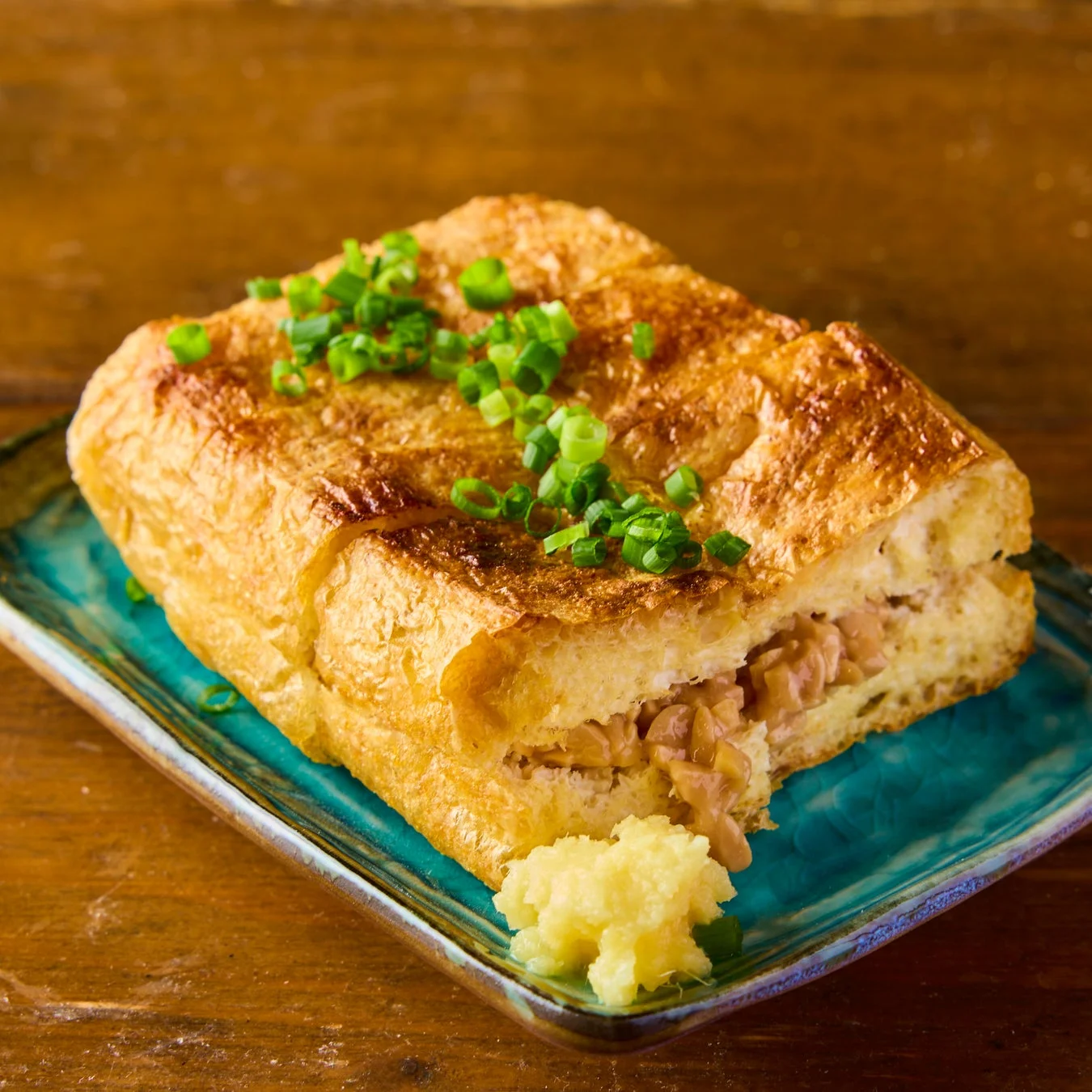 油揚げに納豆を詰めて焼いた料理が、青い皿に盛り付けられています