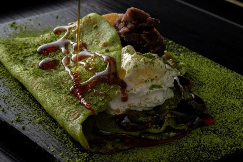 抹茶生地のクレープに、ホイップクリームとあんこが添えられ、上から黒蜜がたっぷりとかけられた和風デザート