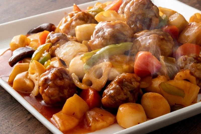熱々の肉団子と蓮根、ピーマン、人参などの彩り豊かな野菜が甘辛いあんかけで絡められた中華風の一皿