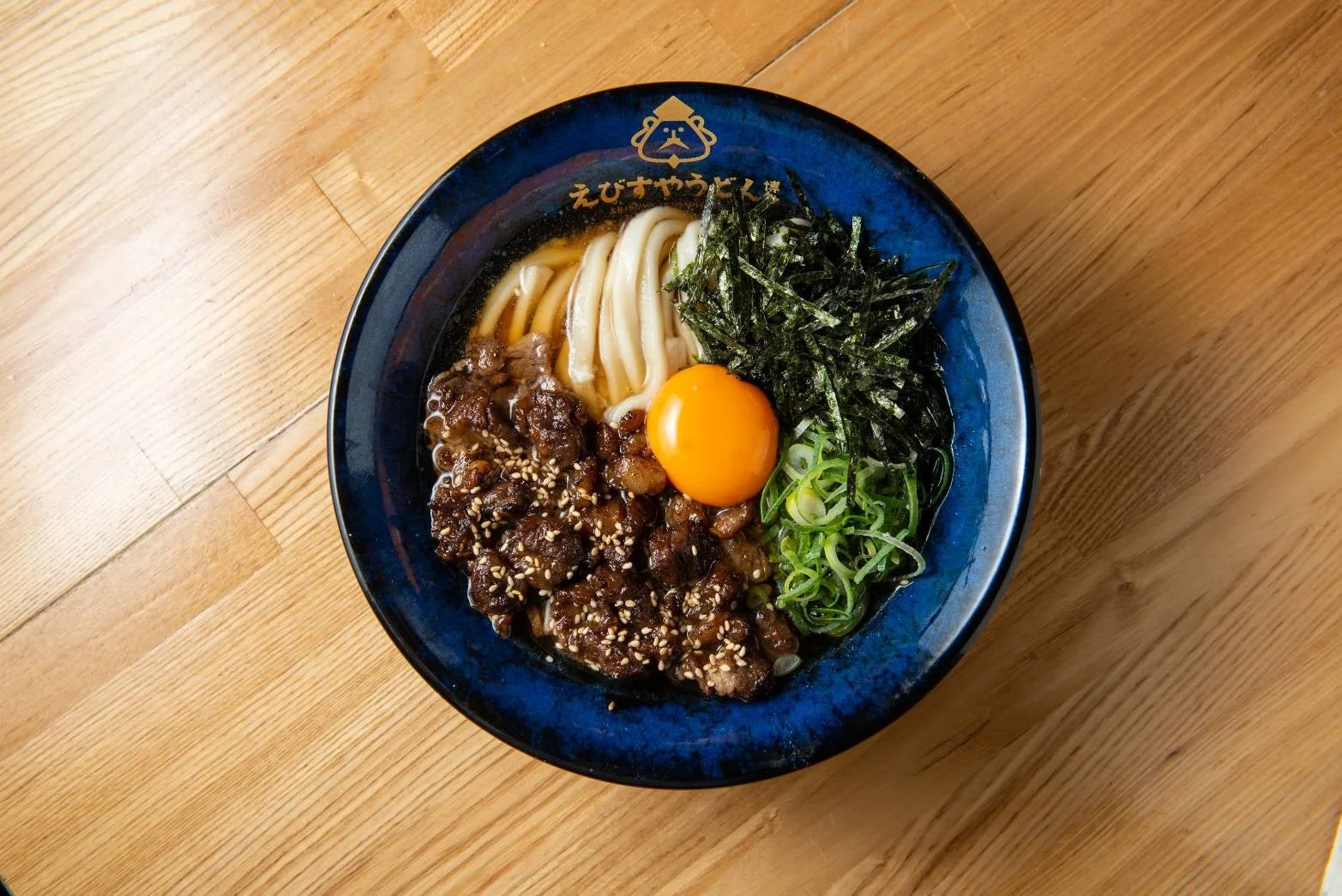 木目のテーブルに置かれた青い器に入ったカルビぶっかけうどん