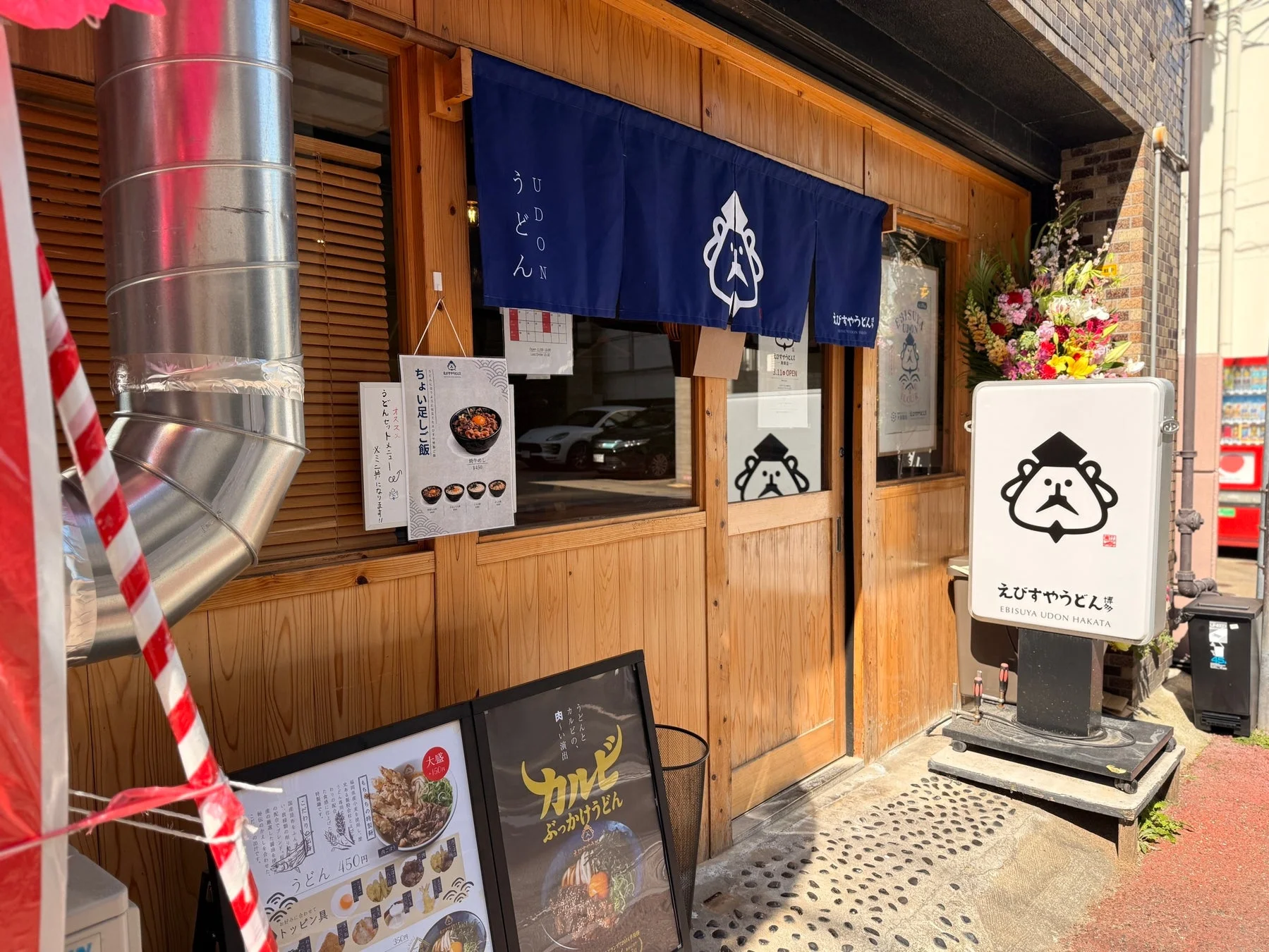 青い暖簾と特徴的なロゴの看板が目を引く「えびすやうどん博多」の店舗外観