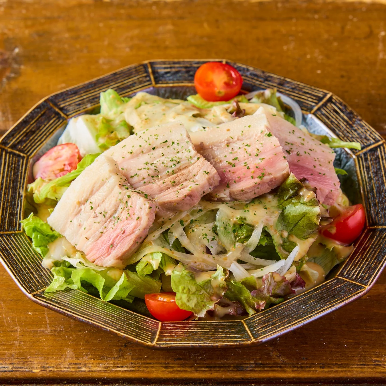 厚切りの豚肉が乗った、レタス、玉ねぎ、ミニトマトなどの新鮮な野菜を使ったサラダです