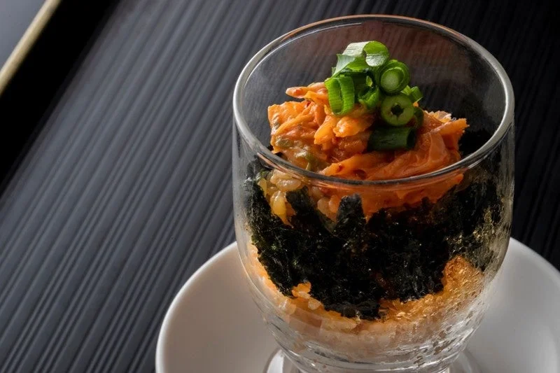グラスに盛り付けられたご飯、海苔、キムチの層にネギが添えられた、彩り豊かな一品