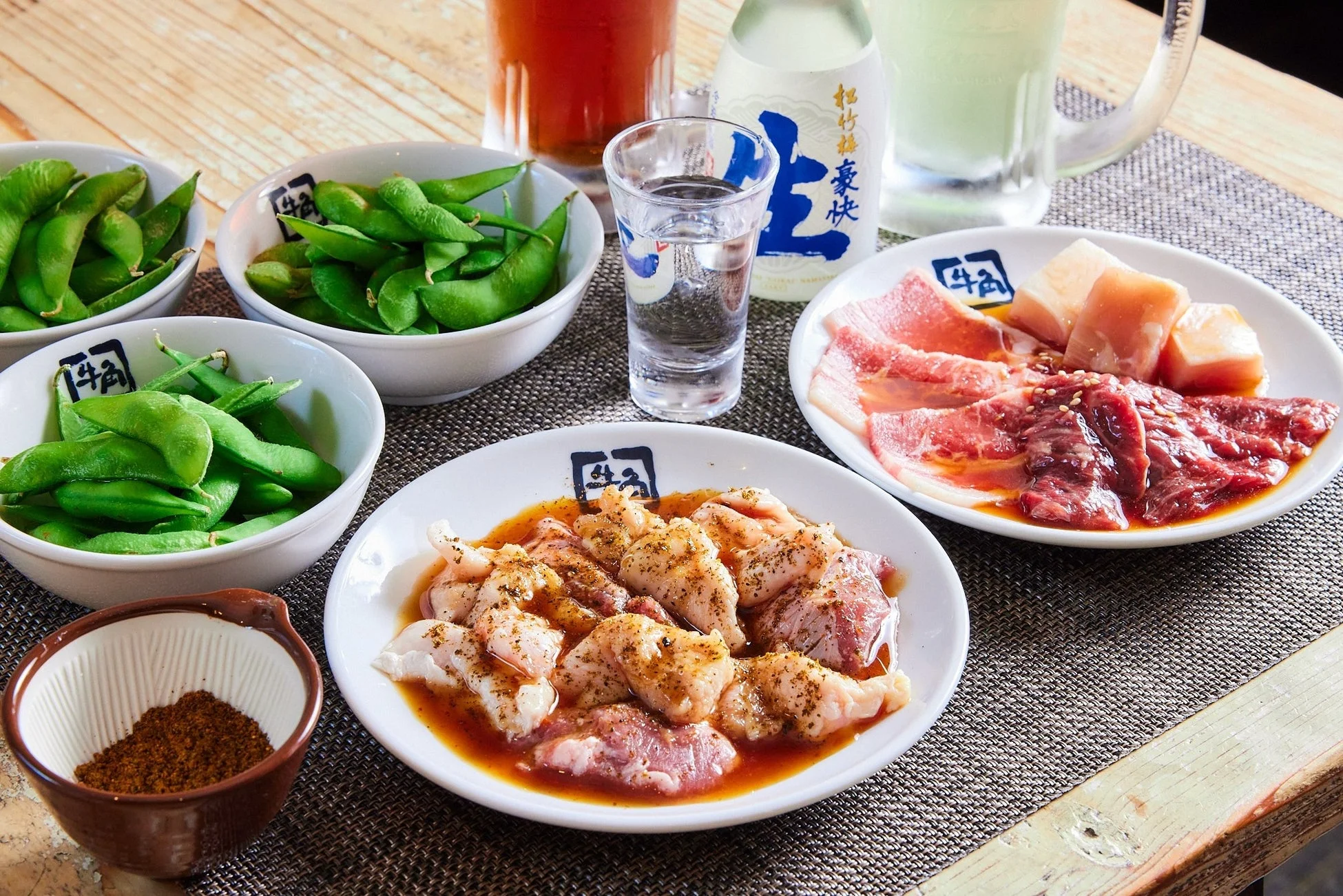 テーブルに並べられた焼肉用の生肉（ホルモン含む）、枝豆、調味料、日本酒やビールなどの飲み物のセット。