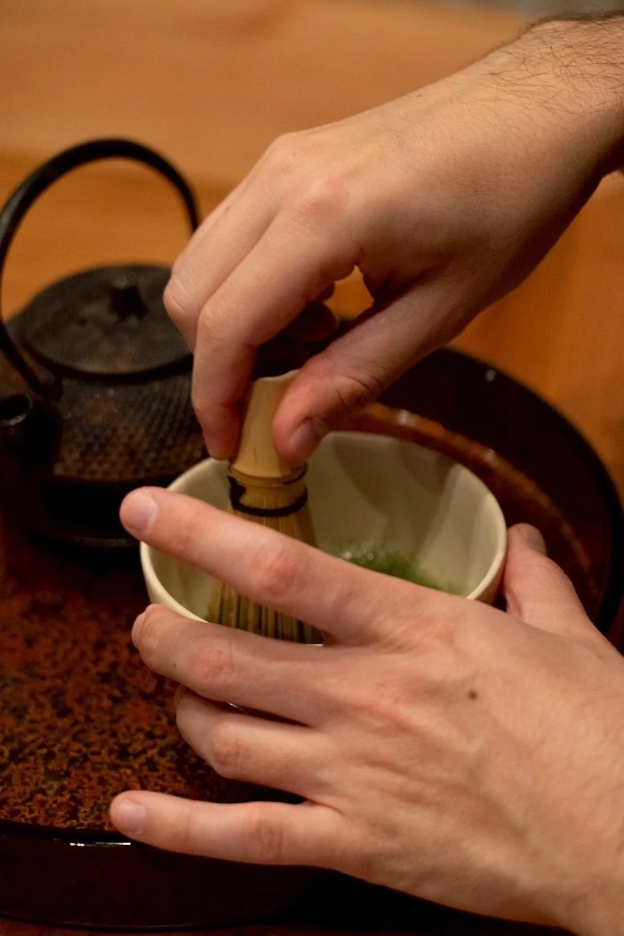 茶碗に入った抹茶を茶筅で点てている様子が写っています。背景には鉄瓶があり、日本の伝統的なお茶の準備風景を表しています。