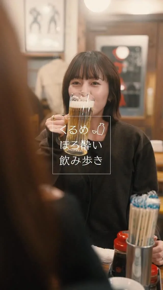 女性が居酒屋でビールジョッキを片手に笑顔で飲んでいる様子