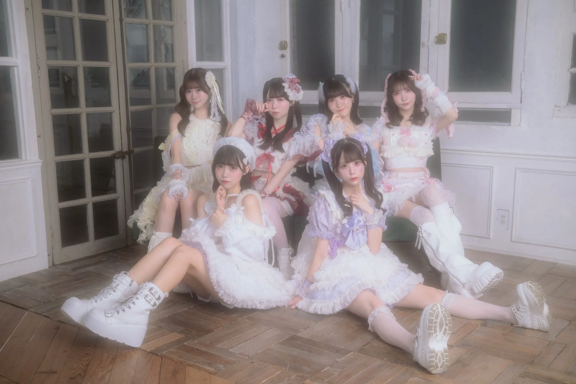 フリルやパステルカラーの可愛らしい衣装を身につけた6人の若い女性が、レトロな雰囲気の屋内でポーズを取っている集合写真。それぞれの個性的なファッションが魅力的な一枚です。