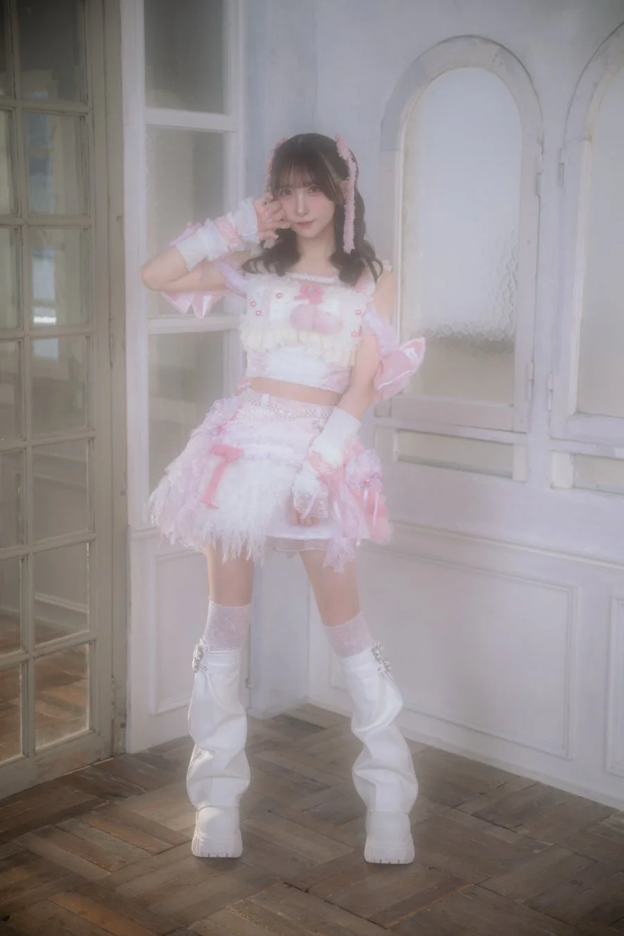 ピンクと白のフリルの衣装を着た若い女性が、窓のある室内でポーズをとっています。全体的に柔らかく夢のような雰囲気です。