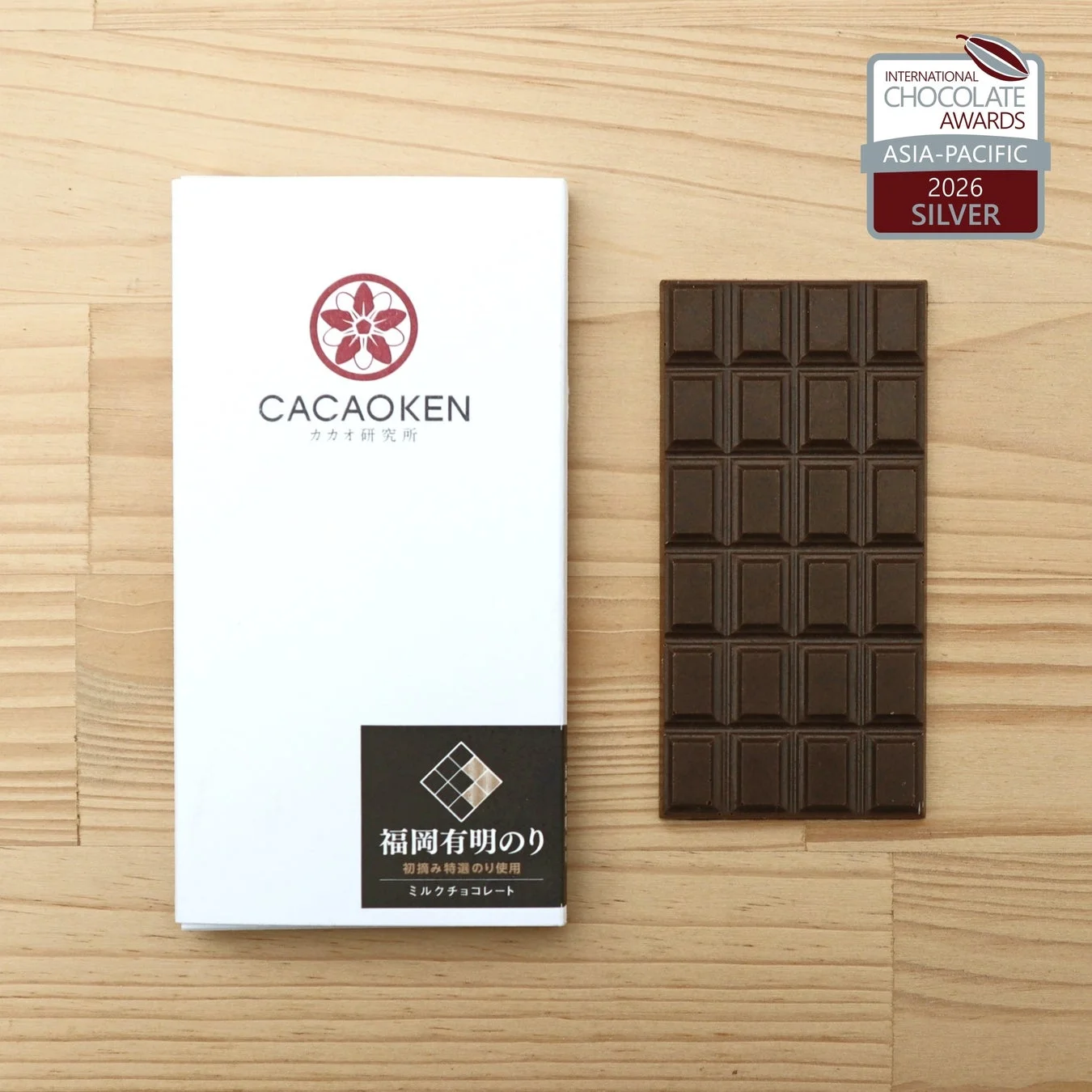 「カカオ研究所」の福岡有明のりミルクチョコレートのパッケージと板チョコが木目の背景に置かれています。国際チョコレートアワード2026アジア太平洋でシルバー賞を受賞したことを示すロゴも写っています。