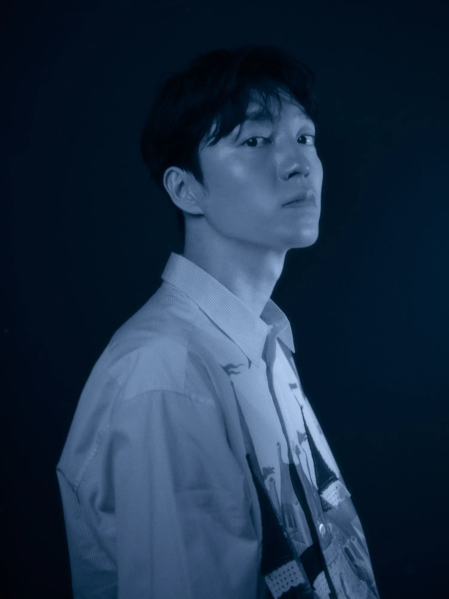 ダークトーンで撮影された男性のポートレート。ストライプシャツを着た男性が、真剣な表情でやや上を見上げている。ドラマチックな照明が印象的。