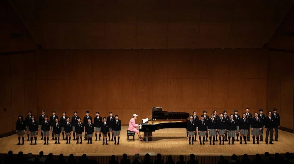 講堂のステージで、制服を着た学生たちが合唱している様子