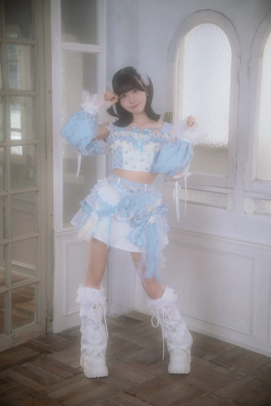 水色と白のフリルが可愛いツーピース衣装を着た若い女性が、明るいスタジオでポーズをとっています。前髪のある黒髪と白い厚底ブーツが特徴的で、全体的に夢可愛らしい雰囲気です。
