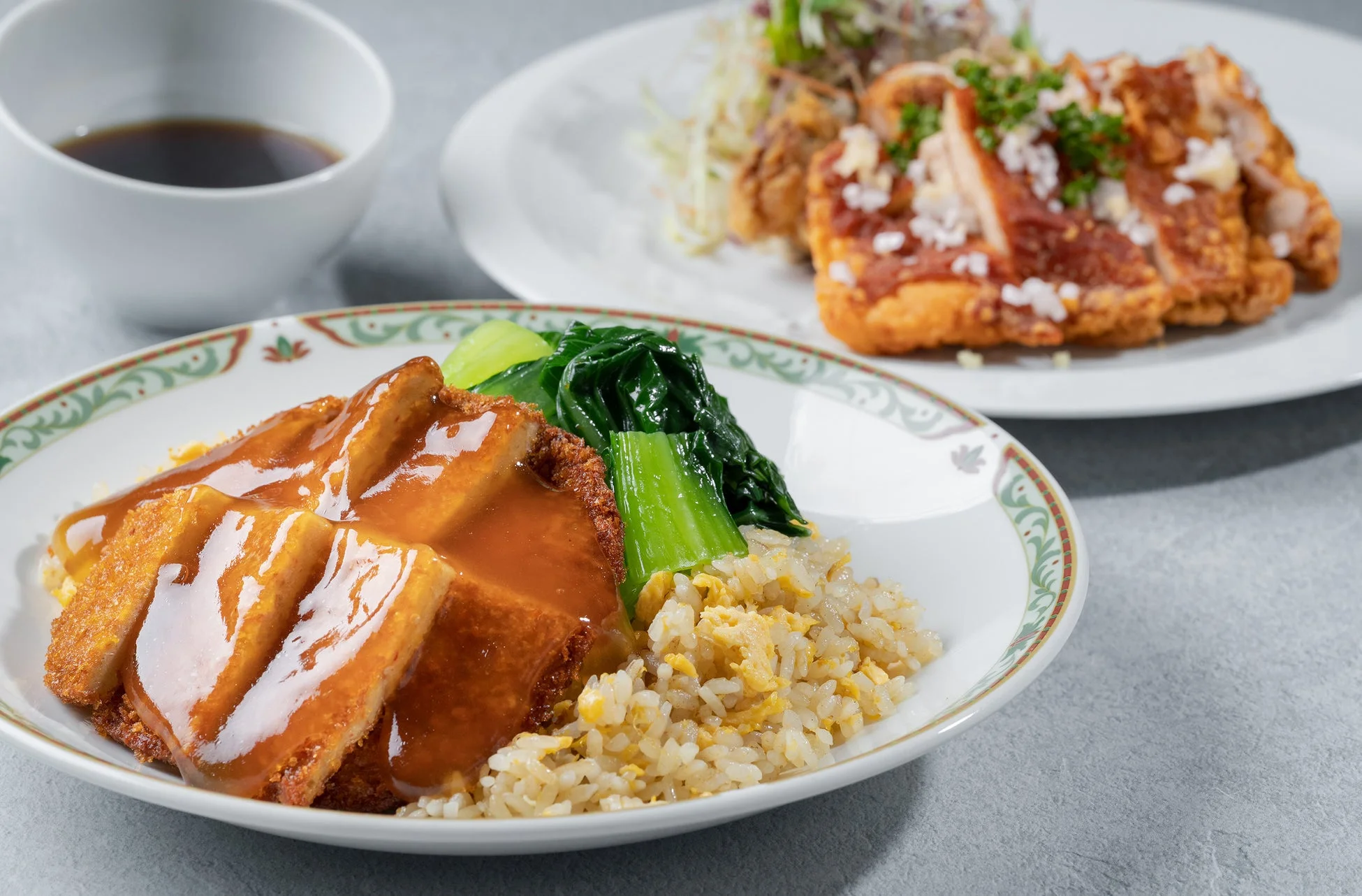 手前にはあんかけソースがかかった揚げ豚肉と炒飯、青菜が盛り付けられたメインディッシュがあり、奥には唐揚げのような揚げ物と小鉢が並ぶ、食欲をそそる定食の様子