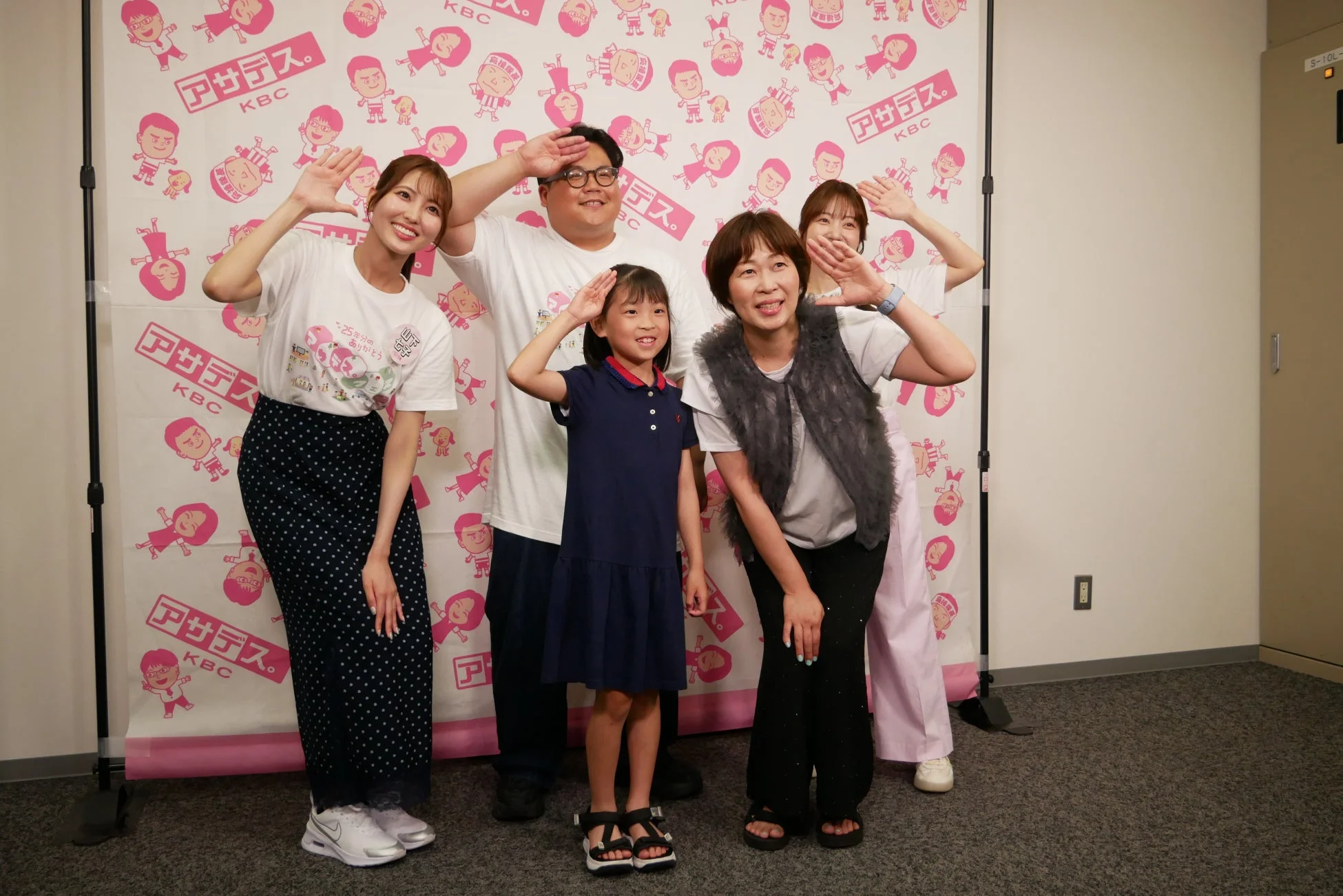 テレビ番組「アサデス。KBC」のロゴ前でポーズをとる人々