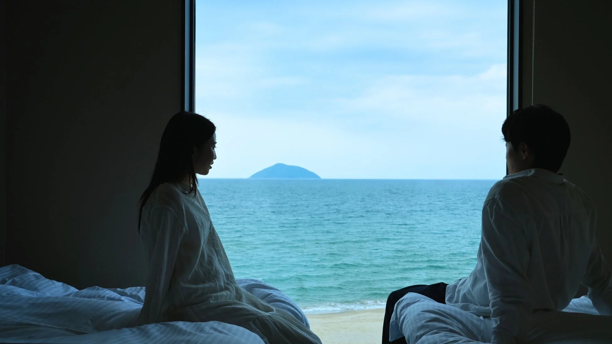 窓から広がる海と遠くの島を眺めるカップルのシルエット
