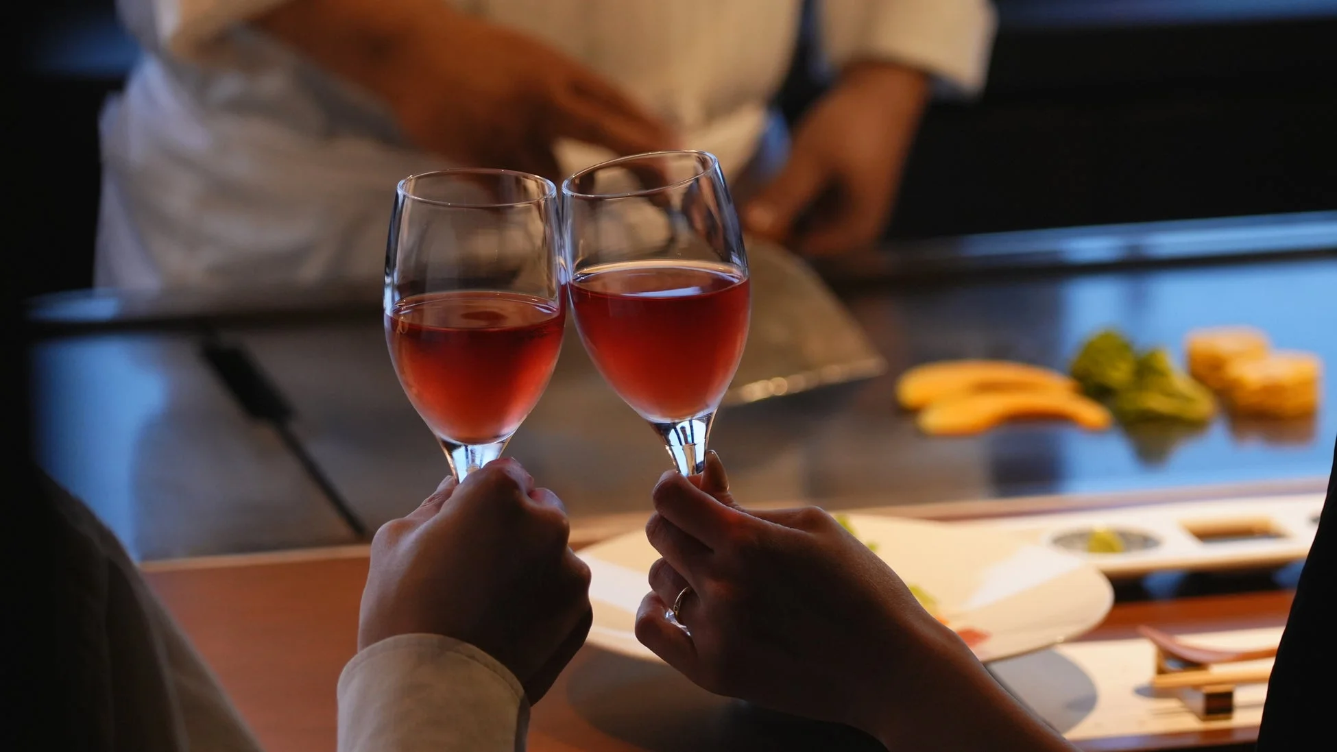 鉄板焼きレストランで、二人が赤い飲み物が入ったグラスで乾杯している瞬間