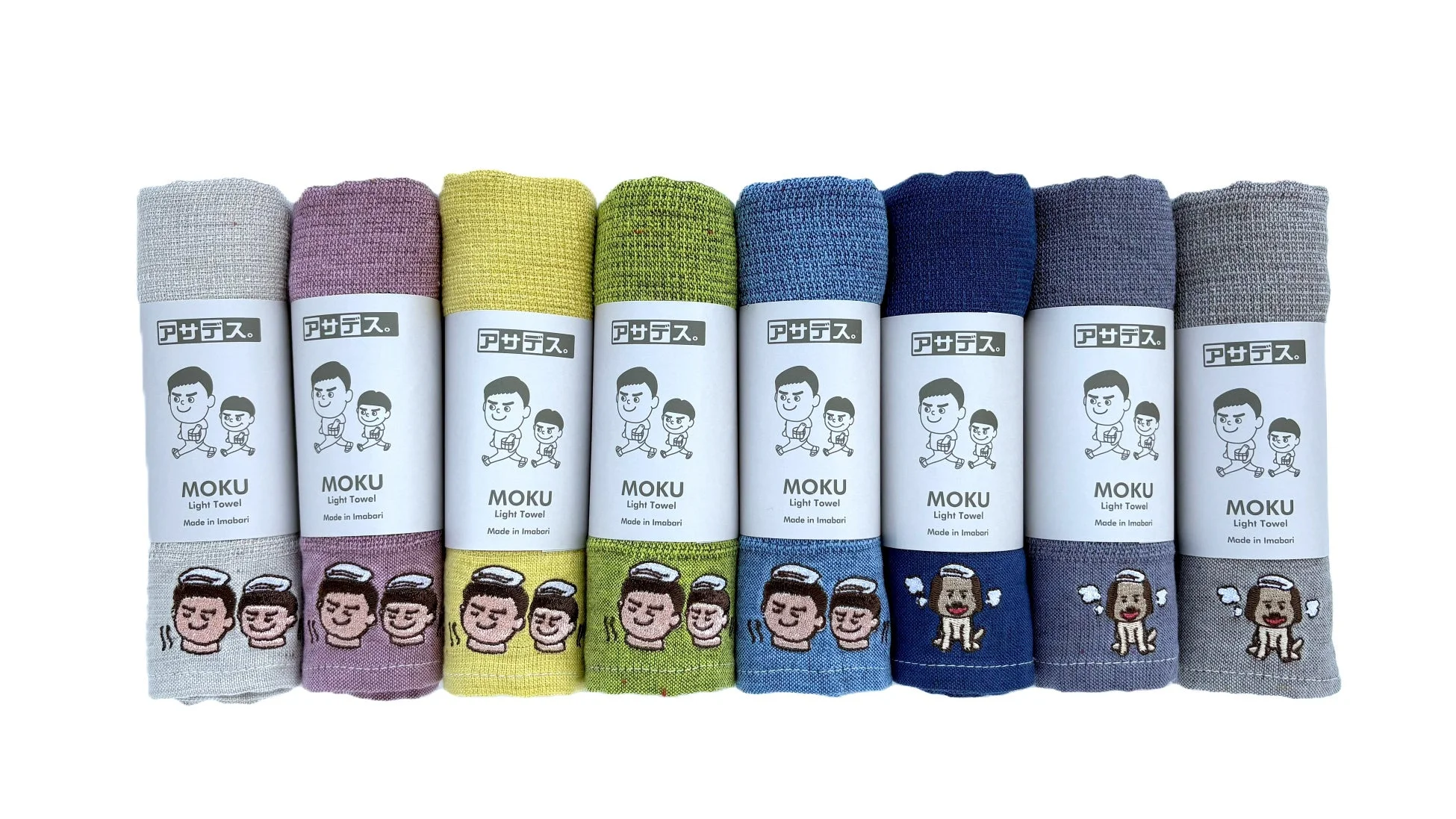 「アサデス。」と「MOKU Light Towel Made in Imabari」のラベルが巻かれた、様々な色の今治タオルが8本並べられています。ラベルには走るキャラクターが描かれ、タオルの下部には顔や犬のようなキャラクターの刺繍が施されています。