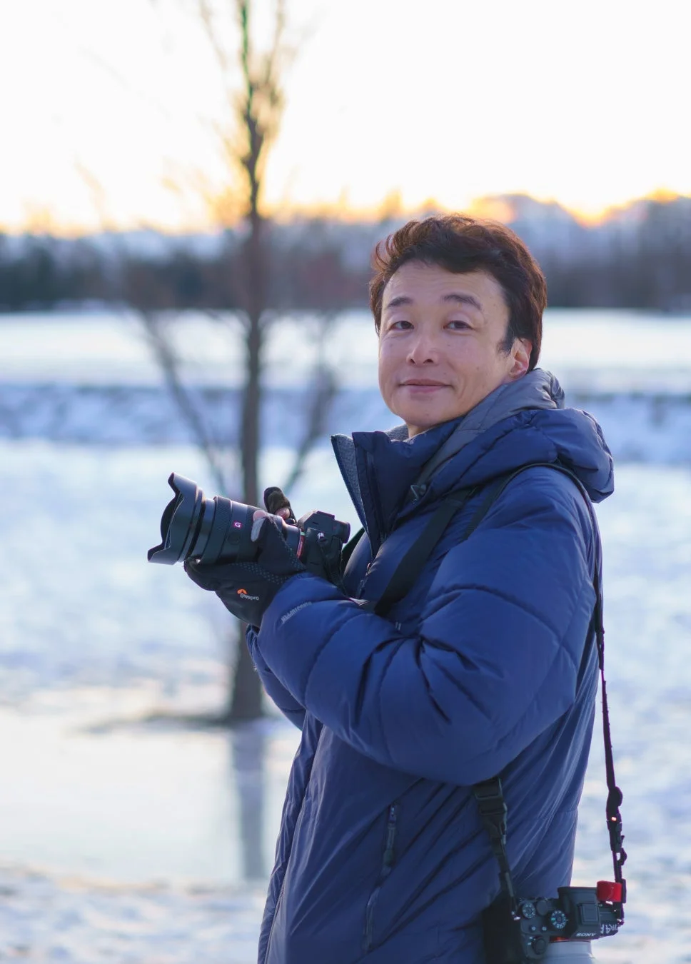 カメラを構え雪景色の中で笑顔を見せるKAGAYA氏