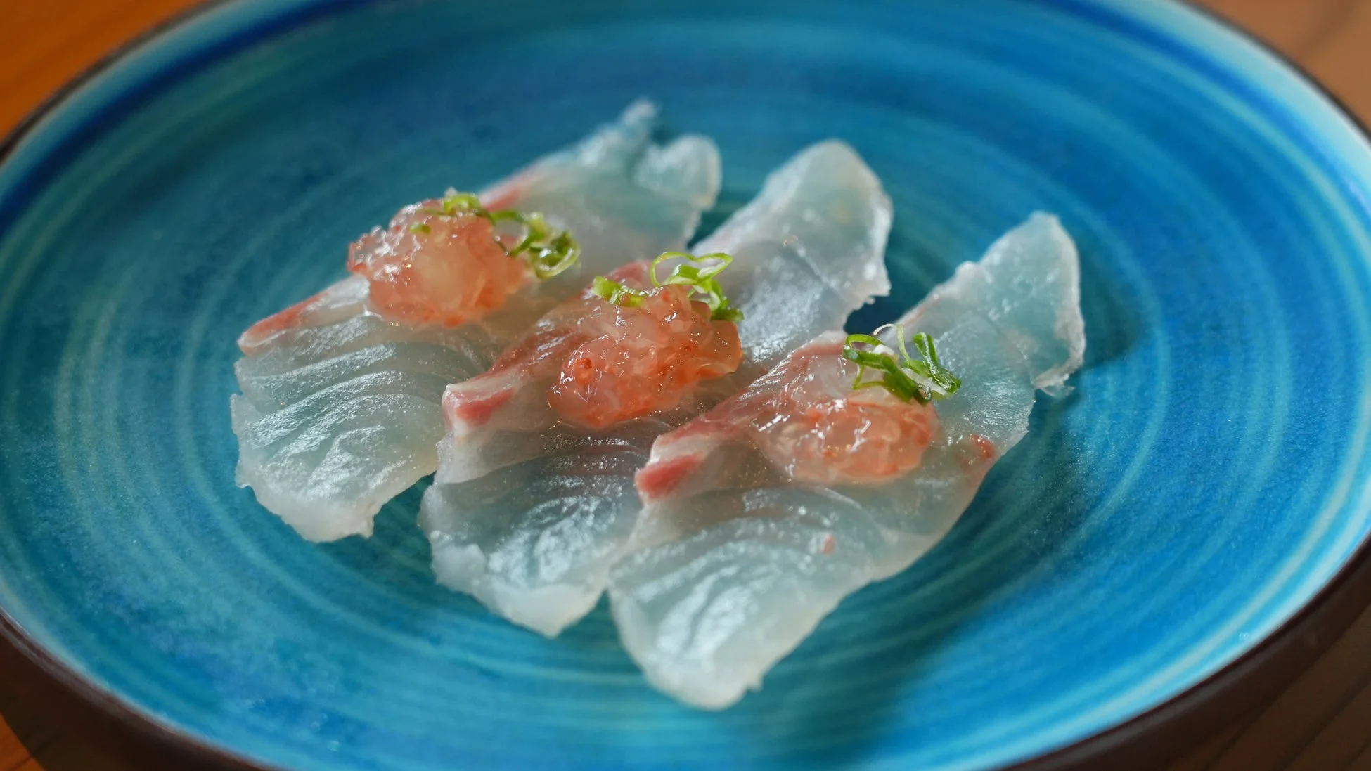 鮮やかな青い皿に盛り付けられた、薄切りの白身魚の刺身