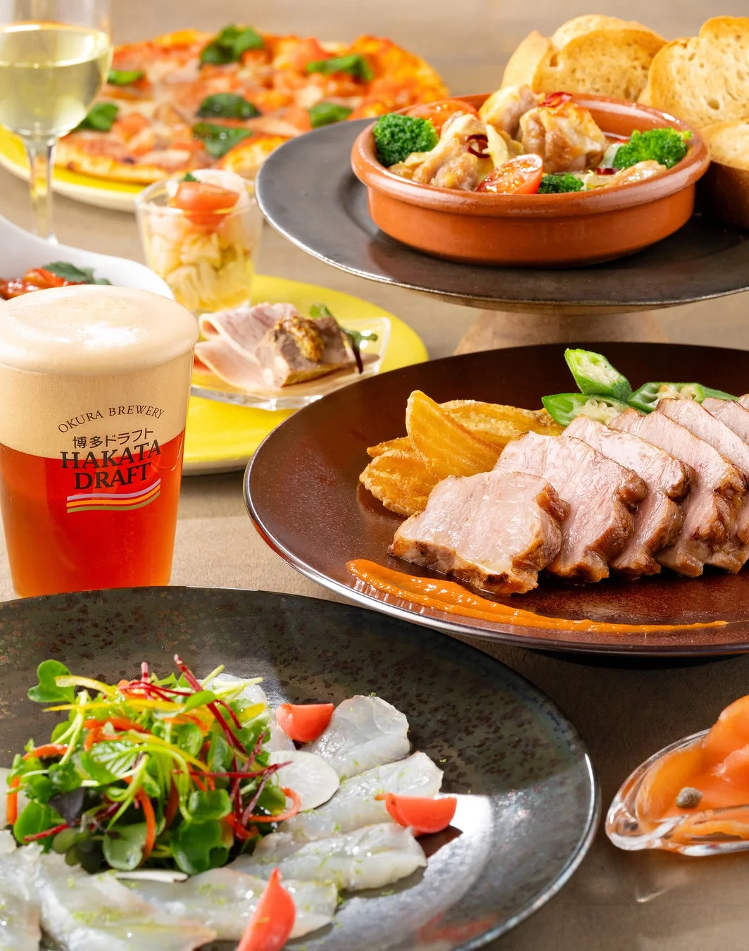 ビールやワイン、ピザ、肉料理など、彩り豊かな洋食が並ぶ食卓の様子