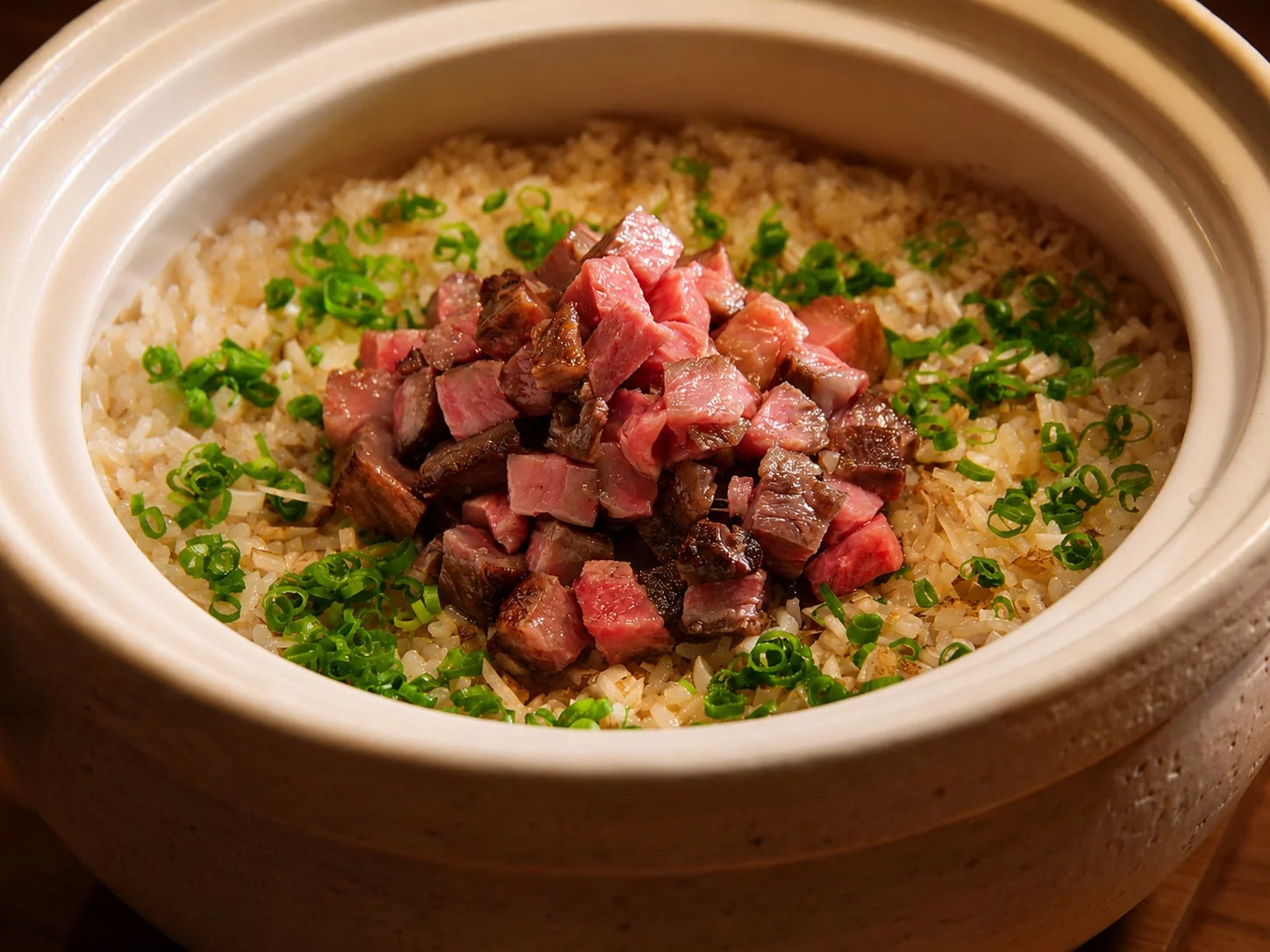 土鍋で炊かれたご飯の上に、サイコロ状にカットされた牛肉と刻みネギがたっぷりと盛り付けられた料理