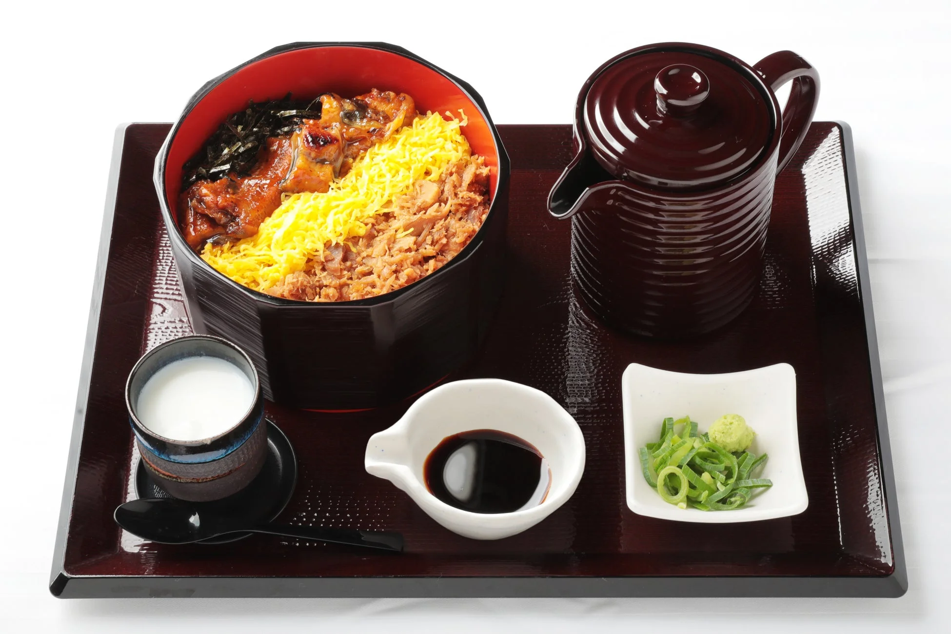 漆塗りのトレーに載せられたひつまぶし風のうなぎ料理と薬味、だし汁のセット。きんしたまごや海苔、ネギ、わさびが添えられ、様々な食べ方で楽しめる和食御膳です。