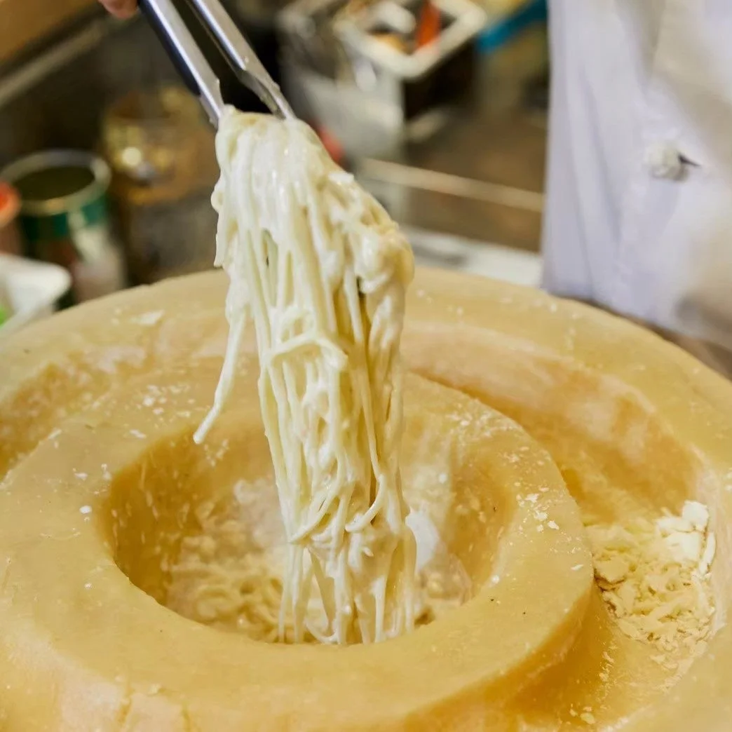 大きなチーズの塊の中で、トングを使ってパスタが混ぜられている様子
